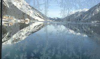 A tranquil lake, surrounded by high mountains and clear sky. Ice crystals adorn the window in the foreground.