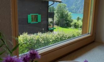 A view from the window of a house with green shutters and a beautiful mountain landscape. In the foreground, there is a purple candle and a few flowers.