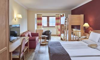 A cozy hotel room with two beds, a seating area, and a window with a view outside. The decor is bright and inviting, perfect for a relaxing stay.