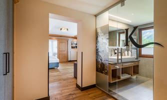 A modern hallway with a wooden floor and large glass wall. On the right side, there is a bathroom with a stylish sink.