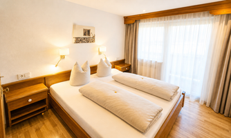 A modern bedroom with a large double bed and two pillows. 

Large windows let in plenty of light and offer a view of the outside surroundings.
