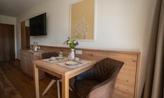 A cozy dining area with a wooden table and chairs. A picture hangs on the wall, and a small flower vase is on the table.