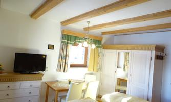A cozy room with a wooden beam ceiling, a table, and chairs. The room contains a television and a large wardrobe.