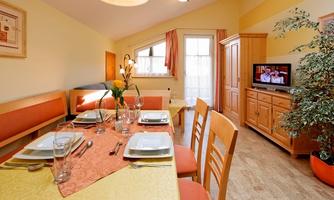 A cozy dining area with a large table and stylish table decoration. In the background, there is a living area and a television.