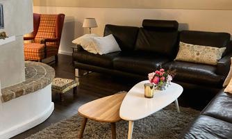 A cozy seating area with a black couch and a stylish coffee table. The room has warm colors and is well-lit, with a view from the windows and a beautiful rug.