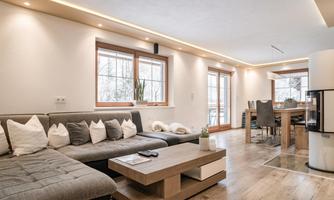 A modern living room with a comfortable sofa and a wooden table. Large windows let in a lot of light and create an inviting atmosphere.