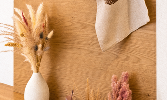A beautiful interior with a wooden background and decorative dried flowers in a vase. Below hangs a linen bag.