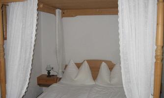 A cozy bedroom with a four-poster bed and white curtains. The beds are neatly decorated with pillows.