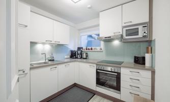 A modern kitchen with white cabinets and a bright countertop. There is a stove, a microwave, and various kitchen appliances.