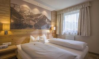 A cozy bedroom with two beds and wooden paneling. There is a picture of a mountain landscape on the wall.