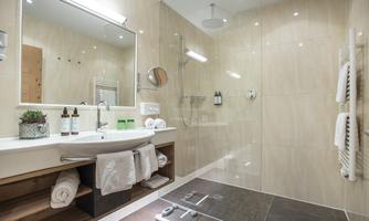A modern bathroom with a walk-in shower and elegant tiles. The decor includes a sink area with towels and toiletries.