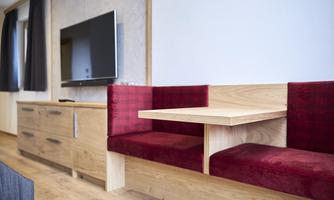 A modern living room with a flat-screen TV and a cozy seating area made of wood and red cushions. The floor is made of light wood and creates a warm atmosphere.