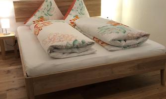 A cozy bedroom with a double bed and decorative pillows. The floor is wooden and the walls are painted light.