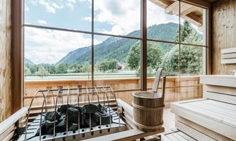 A bright wellness area with a sauna and large window. The view of the green mountains and the sky provides relaxation.