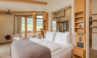 A modern bedroom with a large bed and wooden shelves. The large windows provide a beautiful view of the landscape.