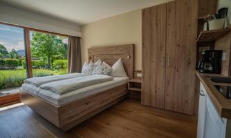 A bright and modern bedroom with a large bed and wooden furniture. The room has large windows overlooking a green garden.