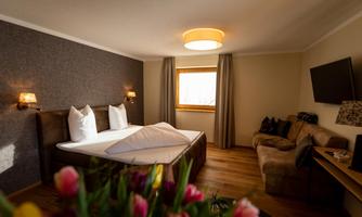 A modern hotel room with a large bed and a cozy sofa. The room features a bright window front and is stylishly decorated.