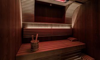 A modern sauna with wooden interior and soft lighting. In the foreground, there is a wooden bucket and a sauna ladle.