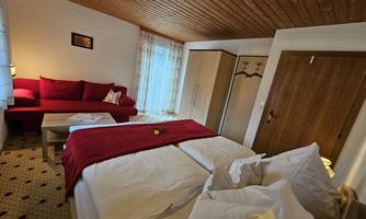 A cozy bedroom with a large bed and a red throw. The room contains a sofa and a wooden wardrobe.