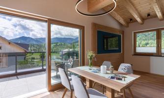A modern living room with a large window that opens up to views of the mountains and nature. The room is bright and welcoming, featuring a wooden log and an elegant dining table.