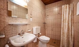 A small bathroom with tiled walls. There is a sink, a toilet, and a shower with a shower curtain.