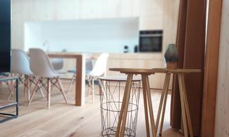 A modern living space with wooden paneling and an elegant kitchen design. In the foreground, there are two stylish side tables.