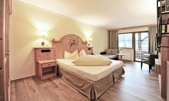 A modern room with wood decor and a cozy bed. Large windows provide plenty of daylight and a view of the surroundings.