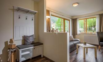 A bright living room with large windows and a view of greenery. A cozy couch and a small table complete the space.