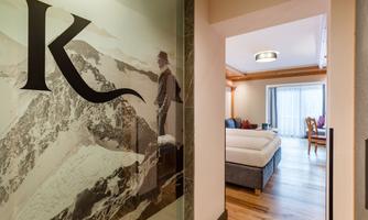 A stylish entrance area featuring a large picture of a mountain and the letter "K". In the background, an inviting bedroom with wooden flooring can be seen.