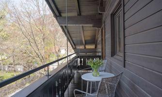 A balcony with wooden cladding and a small table. On the table, there is a vase with tulips, and there is a view of trees in the background.