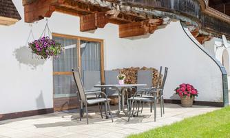 A cozy terrace with a table and chairs. The area is surrounded by green lawn and beautiful flowers.