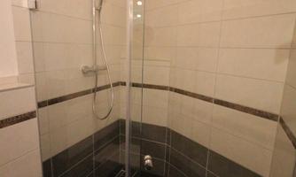 A modern bathroom with a glass shower. The walls are adorned with white tiles and the floors are designed with black tiles.