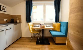 A cozy kitchen corner with a table, two chairs, and light wooden paneling. The room is well-lit with windows and modern furniture.