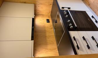 A modern kitchen with a ceramic glass cooktop and an oven. The walls are wooden-paneled and the cabinets have a simple design.