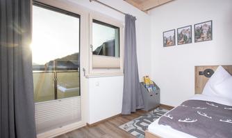 A bright room with a window leading to a balcony. The walls are decorated with photos and there is a cozy bed.