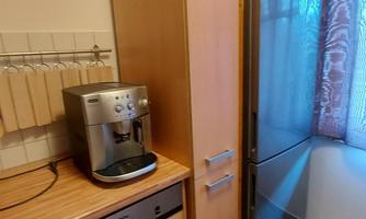 A modern kitchen with wooden cabinets and a refrigerator. On the countertop, there is a coffee machine.