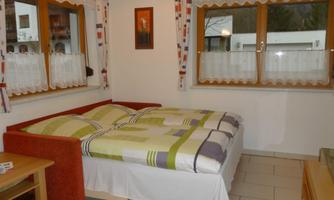 A cozy bedroom with a double bed and colorful bedspreads. There are two windows that let in a lot of light.