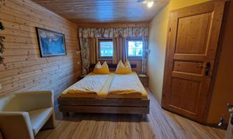 A cozy bedroom with wood paneling and two beds. The room has large windows that let in plenty of light and a friendly atmosphere.