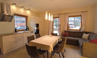 A modern kitchen with a large dining table and cozy chairs. Windows provide a view outside and let in plenty of light.
