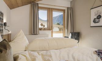A cozy bedroom with a wooden ceiling and large windows. View of the mountains and an inviting bed setup.