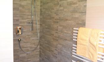 A modern shower with gray tiles and a rain shower. Towels in yellow hang on a towel warmer.