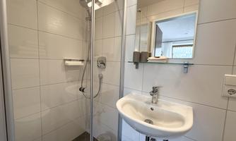 A modern bathroom with a shower, a sink, and a mirror. The walls are tiled with white tiles.
