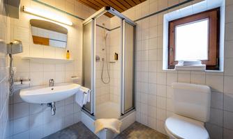 A modern bathroom with a shower, a sink, and a toilet. Large tiles and a window provide brightness.