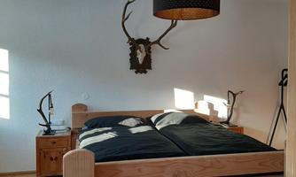 A cozy bedroom with a large wooden bed and dark bed coverings. A trophy and a stylish lampshade hang on the wall.