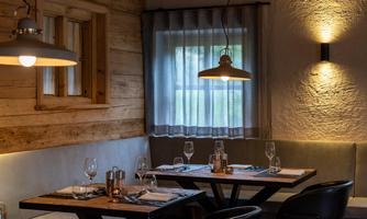 A cozy restaurant with wooden walls and dimmed lighting. Glasses and cutlery are on the tables, and the atmosphere is inviting.