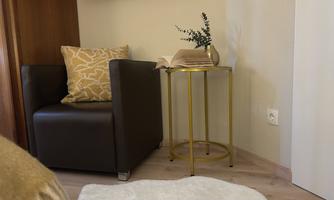 A cozy seating area with a brown armchair and a golden side table. Next to it lies an open book and a small plant.