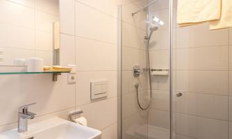 A modern bathroom with a shower and a sink. The walls are tiled in bright colors, and there are fresh towels.