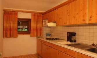A cozy kitchen with wooden cabinets and a light floor. The windows are decorated with colored curtains.