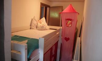 A cozy children's room with a loft bed and a pink play tent corner. The walls are light and there are some Nordic decoration elements.