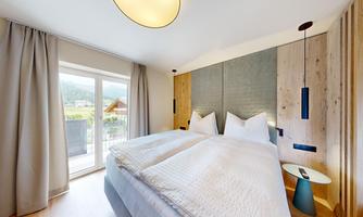 A modern hotel room with two single beds and soft colors. Large windows offer a view of the outside and plenty of daylight.